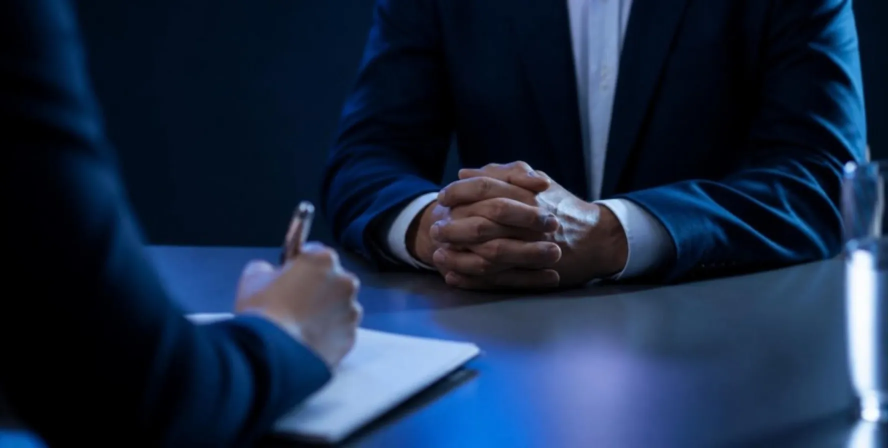 Entretien en tête-à-tête : mains jointes d'un interlocuteur face à une prise de notes